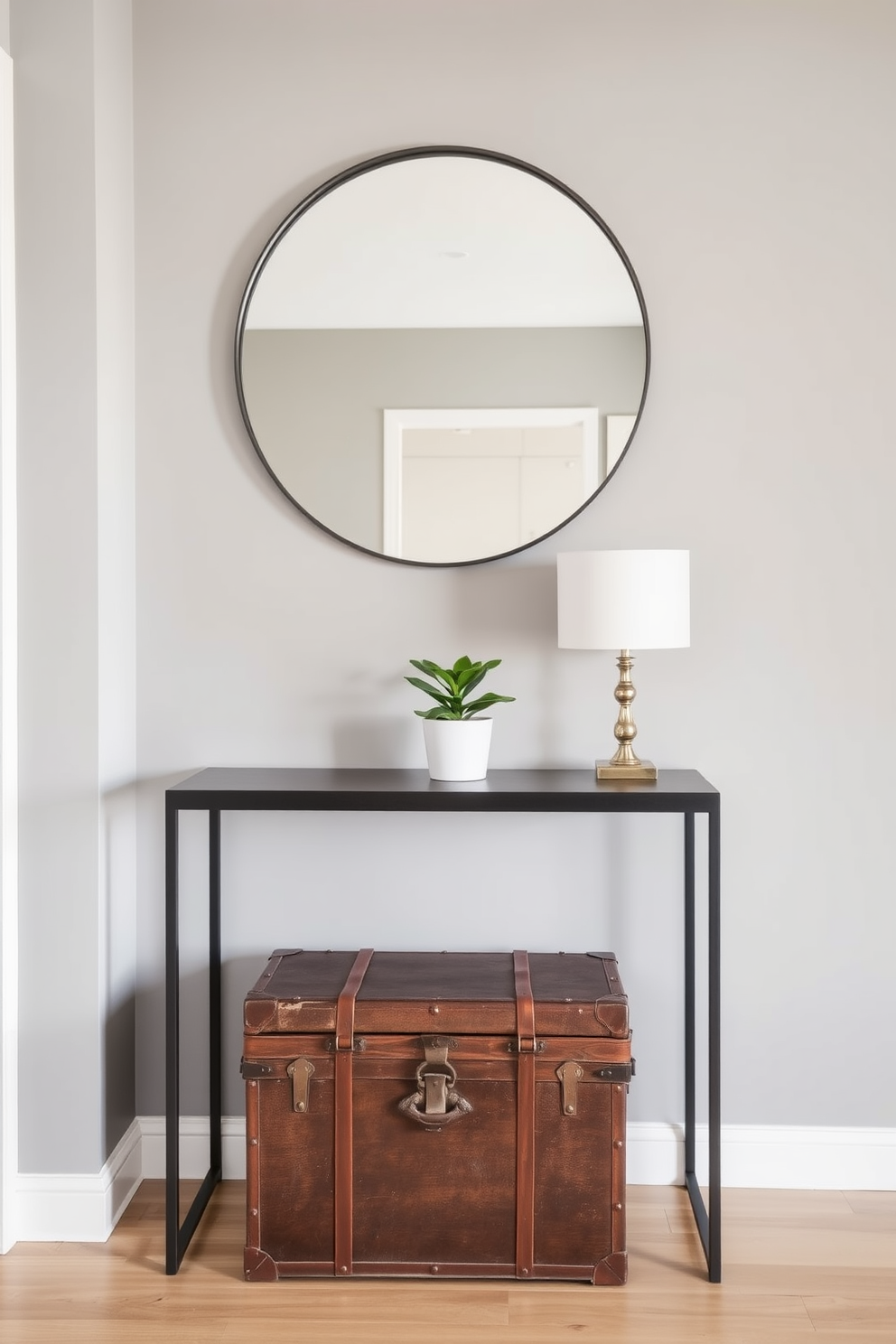 A stylish condo entryway featuring a sleek console table against the wall. Above the table, a large round mirror reflects the space, while a vintage trunk for storage sits at the base, adding character and functionality. The walls are painted in a soft gray tone, creating a warm and inviting atmosphere. A small potted plant sits on the console table, complementing the overall design.