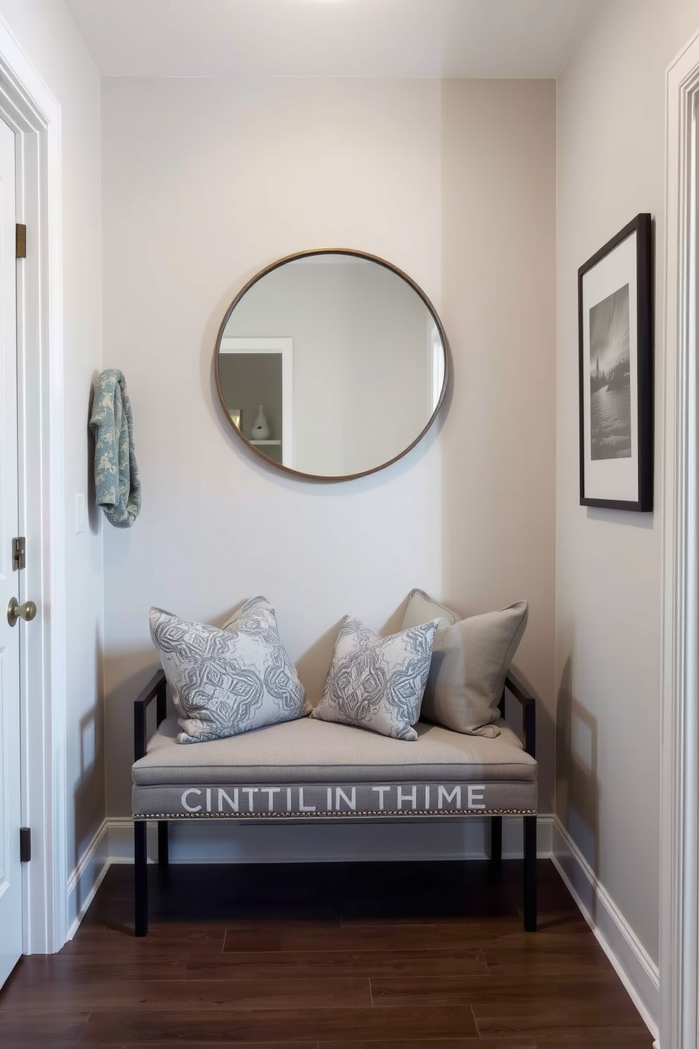 A stylish condo entryway featuring a small bench for seating against a wall. The bench is upholstered in a soft gray fabric with decorative throw pillows, and a round mirror hangs above it, reflecting natural light.