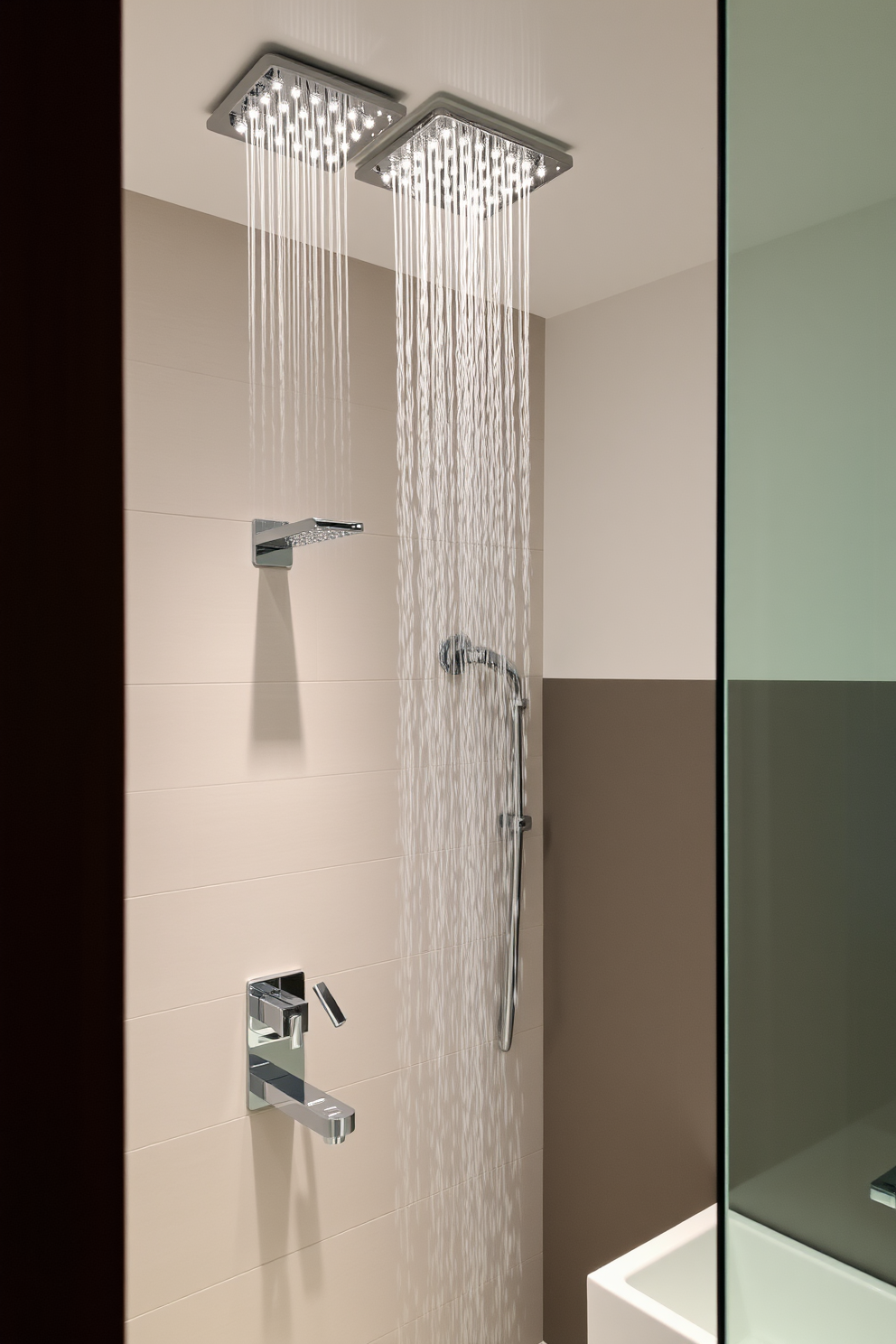 A contemporary bathroom featuring elegant rain shower heads that create a luxurious atmosphere. The space is adorned with sleek tiles and modern fixtures, emphasizing a clean and sophisticated aesthetic.