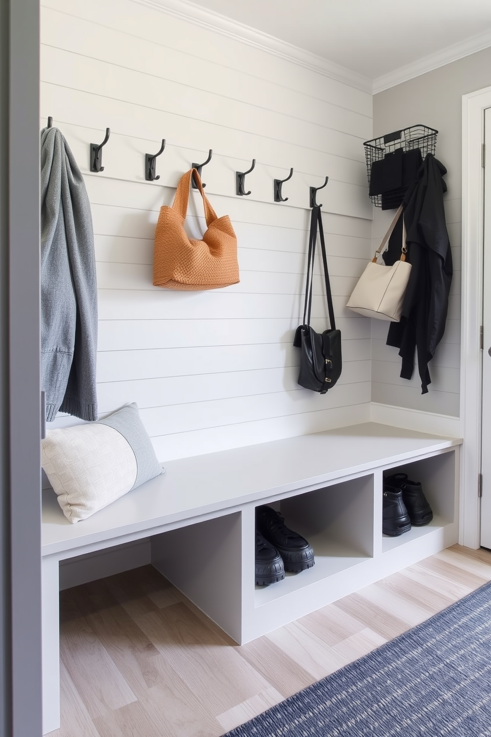 A functional seating area in a contemporary mudroom features a sleek bench with built-in hidden storage underneath. The walls are adorned with light gray shiplap, and there are hooks above the bench for hanging coats and bags.