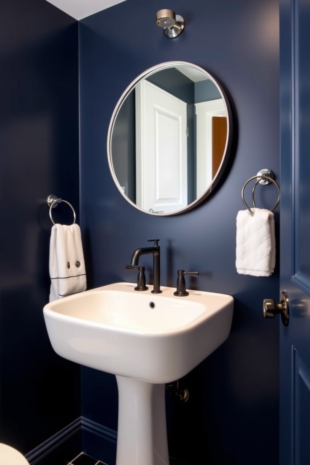 A contemporary powder room featuring high-contrast fixtures that create a striking appearance. The walls are painted in a deep navy blue while the fixtures are in polished chrome for a bold contrast. A sleek pedestal sink is paired with a modern black faucet, enhancing the room's sophistication. Above the sink, a large round mirror with a thin metallic frame reflects the stylish ambiance of the space.