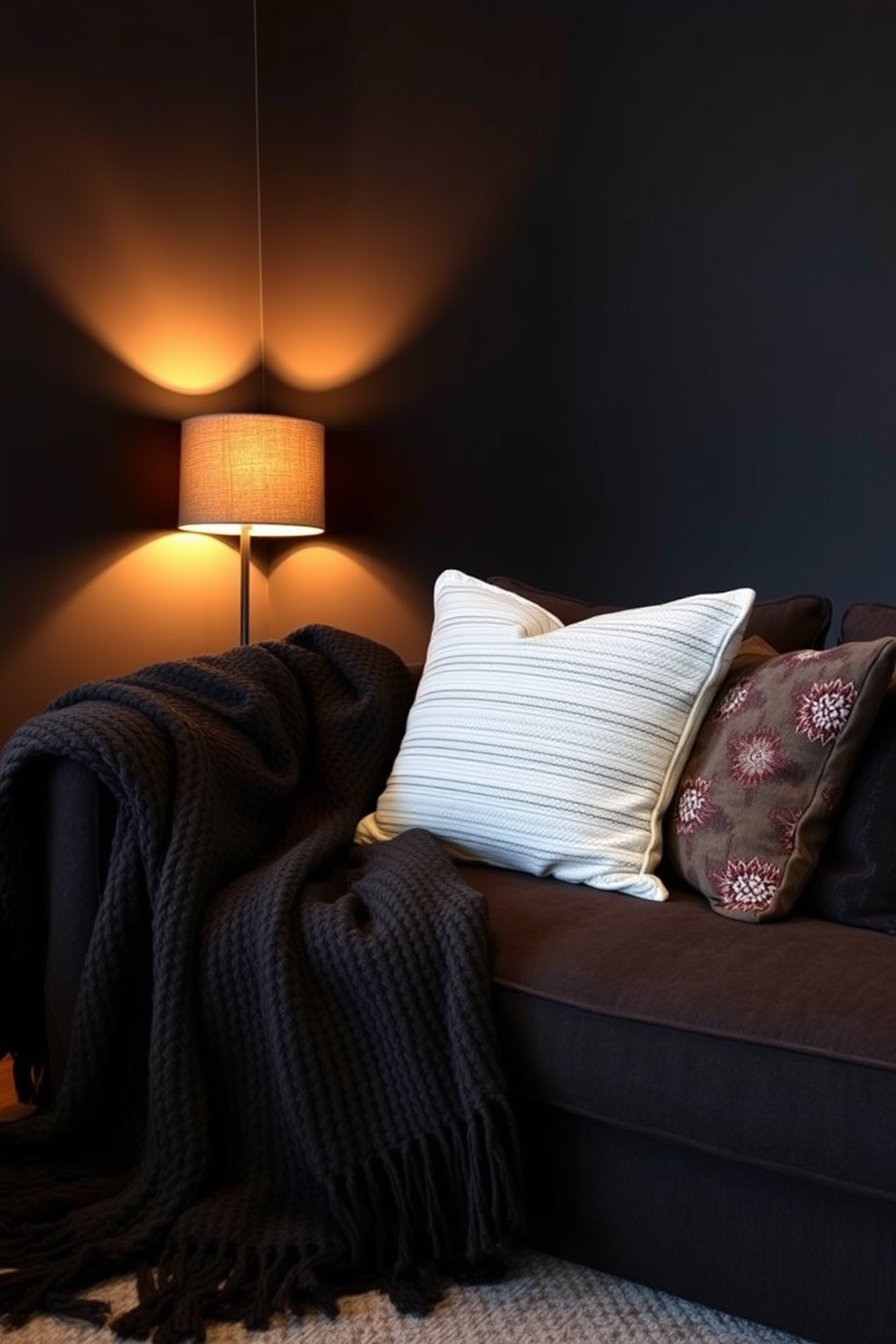 A cozy dark apartment setting featuring rich textured throws draped over a plush sofa. The walls are painted in deep charcoal, and warm ambient lighting casts a soft glow, enhancing the inviting atmosphere. In the corner, a stylish floor lamp with a warm-toned shade illuminates a small reading nook adorned with a textured throw blanket. An eclectic mix of decorative pillows adds depth and comfort to the seating area, creating a perfect space for relaxation.