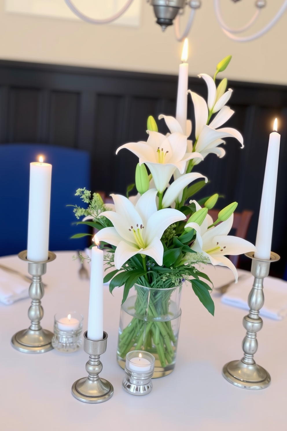 A simple yet elegant floral centerpiece adorns the dining table, featuring white lilies and soft greenery arranged in a clear glass vase. Surrounding the centerpiece, delicate silver candle holders with white candles create a warm and inviting atmosphere for Hanukkah celebrations.