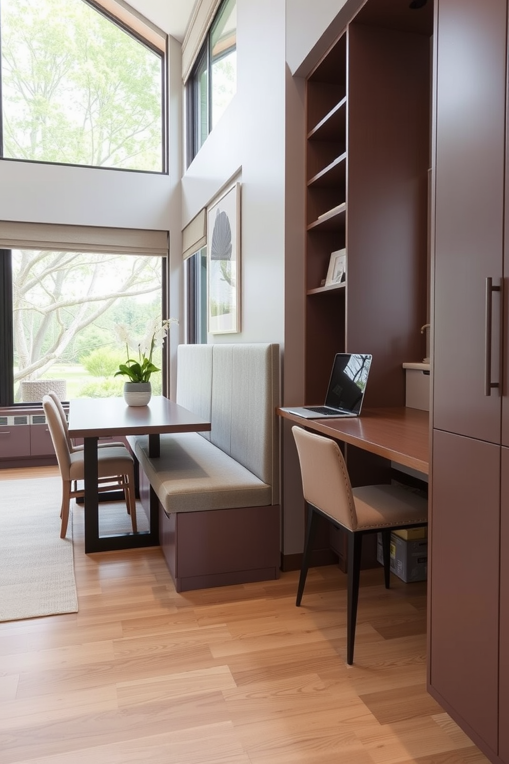 A stylish dining room office combo features a long dining bench with integrated storage underneath. The bench is upholstered in a soft gray fabric, providing comfort while maintaining a sleek appearance. Adjacent to the dining area, a modern desk is seamlessly incorporated into the design, with matching cabinetry that offers additional storage. Large windows allow natural light to flood the space, enhancing the inviting atmosphere.