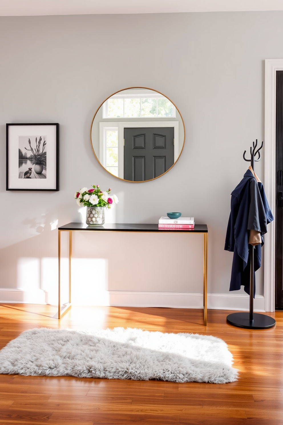 A stylish entryway features a sleek console table against a soft gray wall adorned with framed artwork. A large round mirror hangs above the table, reflecting natural light from a nearby window, while a chic vase with fresh flowers adds a pop of color. The floor is covered in a warm wooden finish, complemented by a plush area rug that invites guests in. To the side, a stylish coat rack holds a few well-coordinated jackets, enhancing the organized yet inviting atmosphere.