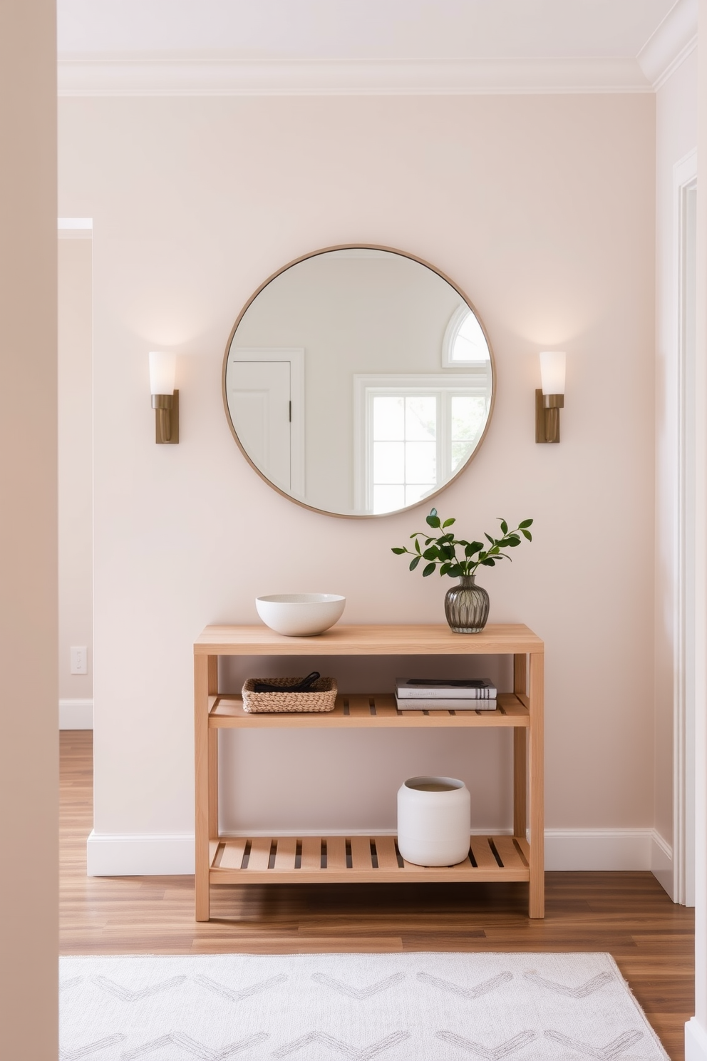 A serene entrance foyer featuring a neutral color palette that promotes a calming vibe. The walls are painted in soft beige, complemented by a light wood console table adorned with a simple decorative bowl and a small potted plant. A plush area rug in muted tones anchors the space, while a pair of elegant wall sconces provide warm lighting. A large round mirror hangs above the console, reflecting the natural light that floods in from a nearby window.