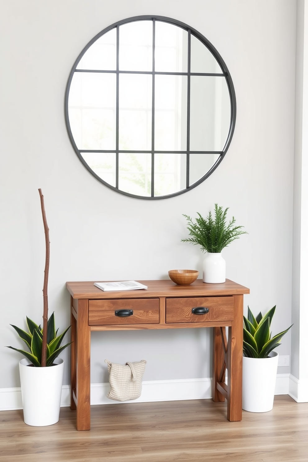 A functional entryway table with drawers sits against a light gray wall. The table is made of reclaimed wood and features a rustic finish, providing ample storage for keys and mail. Above the table, a large round mirror with a black frame reflects natural light. Flanking the table are two stylish potted plants that add a touch of greenery to the space.