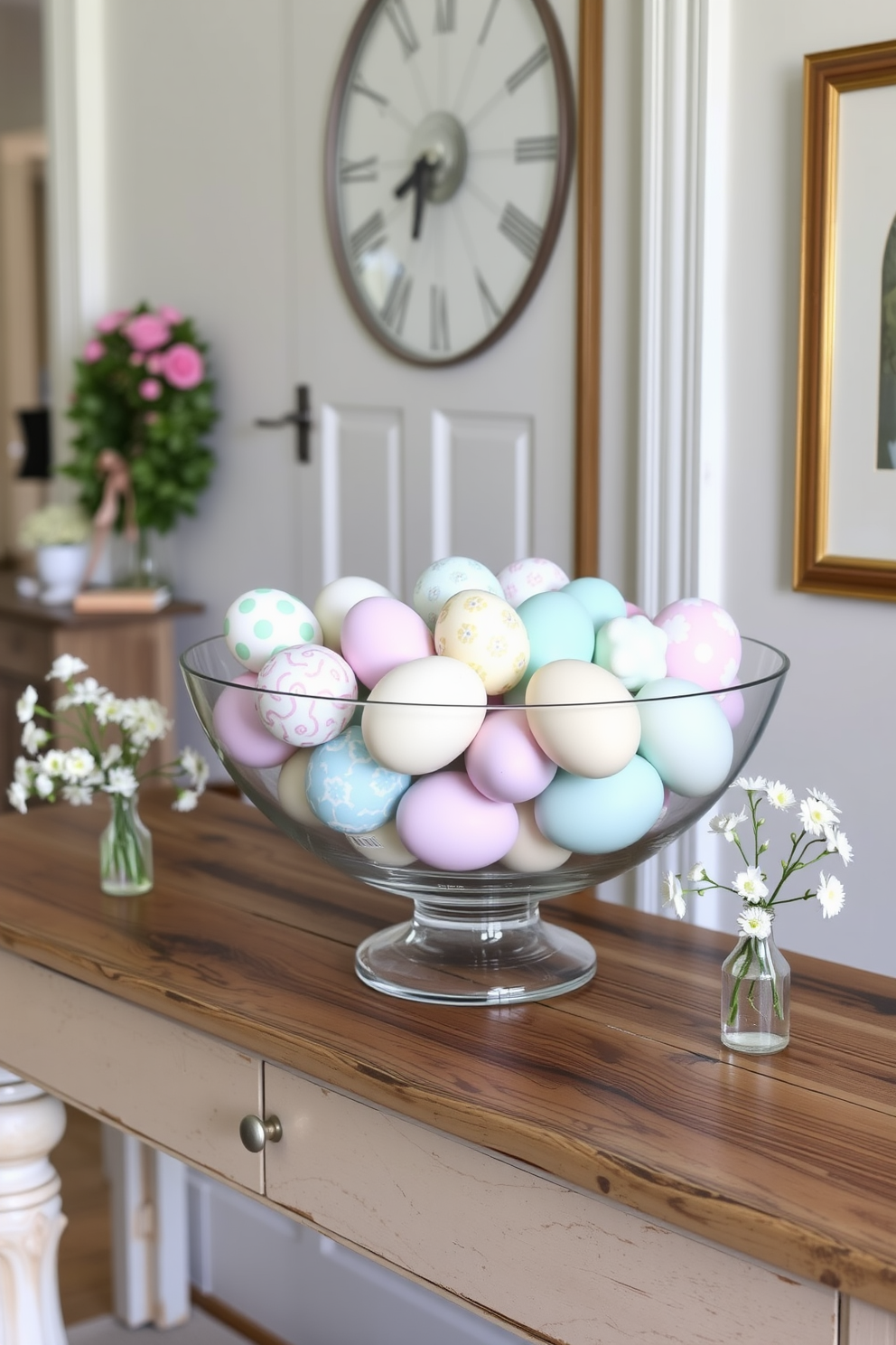 A charming entryway features a large glass bowl filled with an assortment of beautifully decorated Easter eggs in pastel colors. The bowl is placed on a rustic wooden console table, surrounded by delicate spring flowers in small vases.