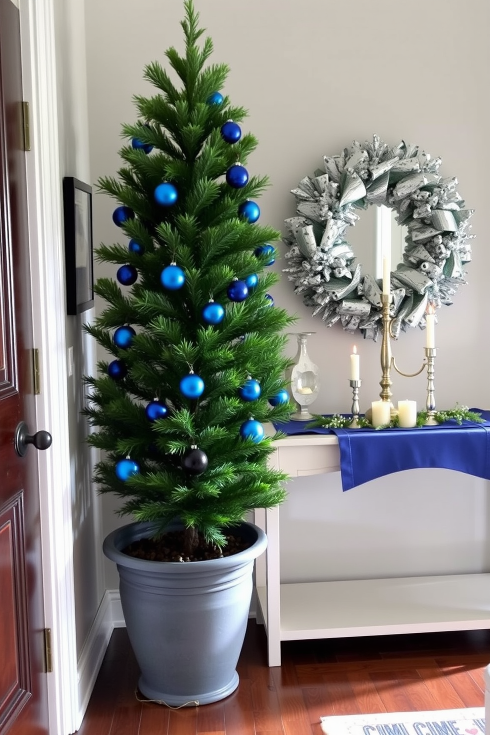 A stylish entryway adorned for Hanukkah features a potted evergreen tree decorated with blue ornaments. The tree is placed near a console table, which is topped with candles and a festive runner, creating a warm and inviting atmosphere.