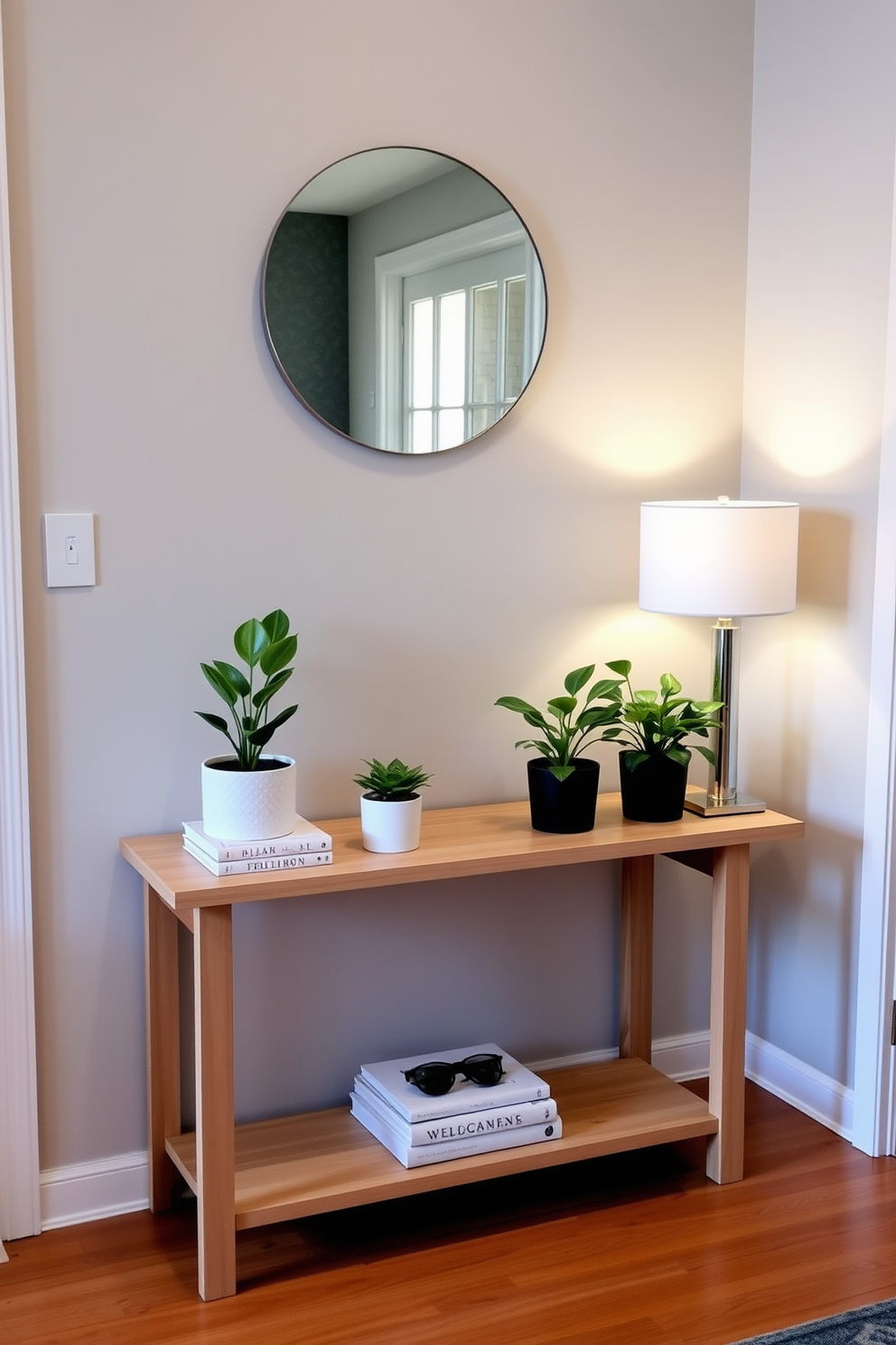 Small potted plants arranged on a sleek entryway table create a welcoming atmosphere. The table features a minimalist design with a light wood finish and a few decorative books stacked neatly. A stylish lamp with a soft glow sits at one end of the table, illuminating the space. Above the table, a round mirror reflects natural light, enhancing the overall brightness of the entryway.