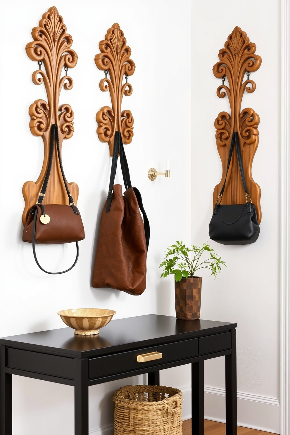 Artistic wall hooks made from natural wood with intricate carvings are mounted on a soft white wall. They provide both functionality and a touch of elegance, perfect for hanging coats and bags. A stylish entryway table features a sleek black finish with gold accents, topped with a decorative bowl and a small potted plant. Underneath, a woven basket adds storage while enhancing the overall aesthetic.