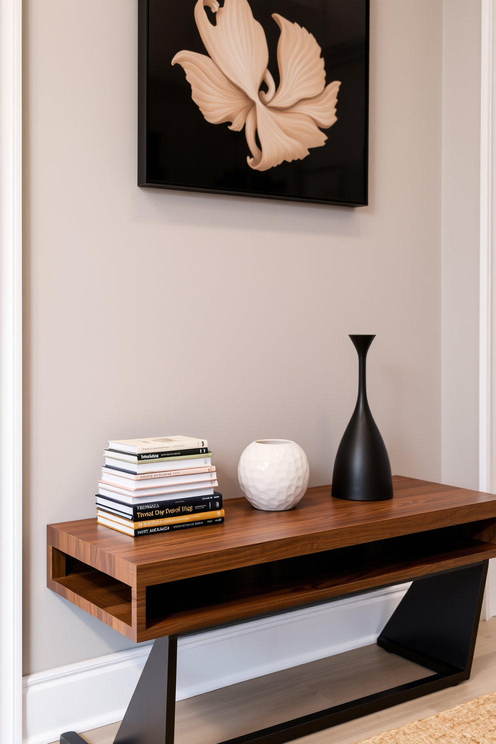 A stylish entryway table features a stack of layered books artfully arranged beside a unique decorative object. The table is made of sleek wood with a minimalist design, and the wall above it is adorned with an elegant piece of artwork that complements the overall aesthetic.