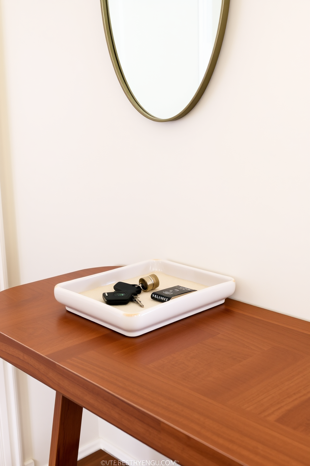 A chic entryway table featuring a sleek wooden surface with a glossy finish. On top of the table, there is a stylish tray made of ceramic in a neutral color, holding keys and small essentials for convenience. The backdrop consists of a soft pastel wall color that enhances the table's elegance. A decorative mirror with a thin metallic frame hangs above the table, adding depth and style to the entryway.