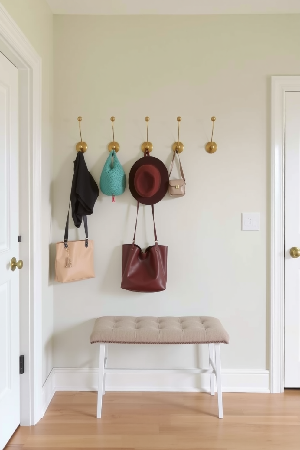 A stylish entryway featuring decorative hooks for hats and bags. The wall is adorned with a soft pastel color, complemented by a chic bench underneath the hooks. Incorporating a mix of modern and rustic elements, the hooks are made of brushed brass. The floor is finished with light hardwood, enhancing the inviting atmosphere of the space.