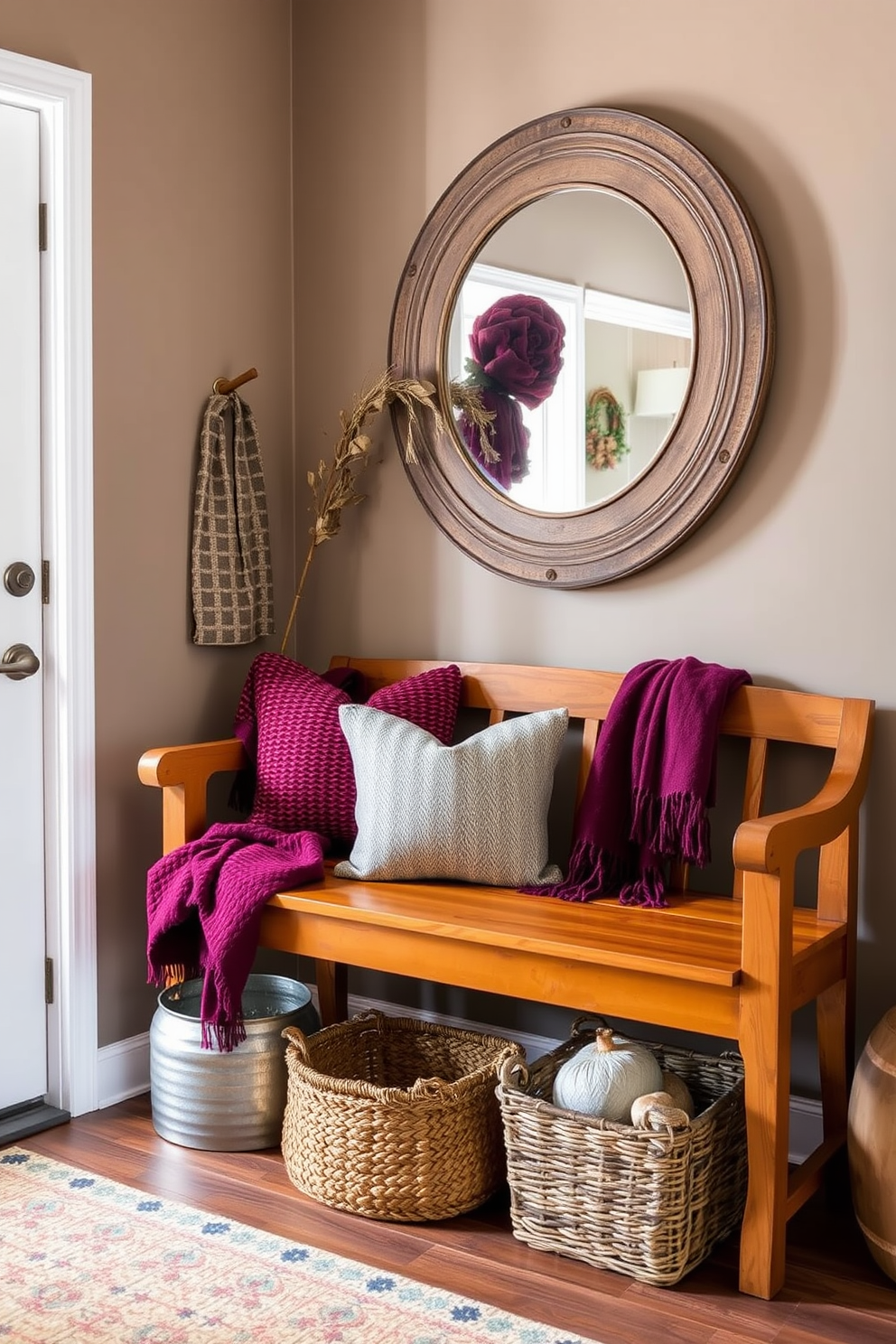 A cozy fall entryway featuring a warm wooden bench adorned with textured throws in rich jewel tones. The walls are painted in a soft taupe, and a large mirror with a rustic frame reflects the welcoming atmosphere.