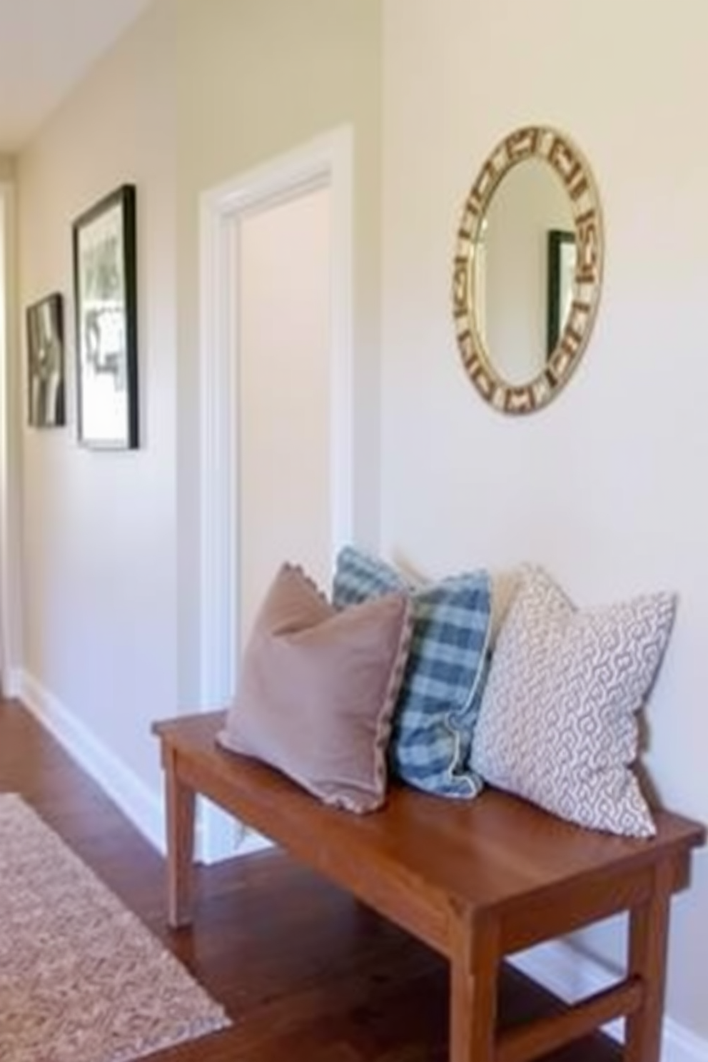 A welcoming hallway features a wooden bench adorned with cozy throw pillows in soft, inviting colors. The walls are decorated with framed artwork and a stylish mirror, creating a warm and inviting atmosphere.