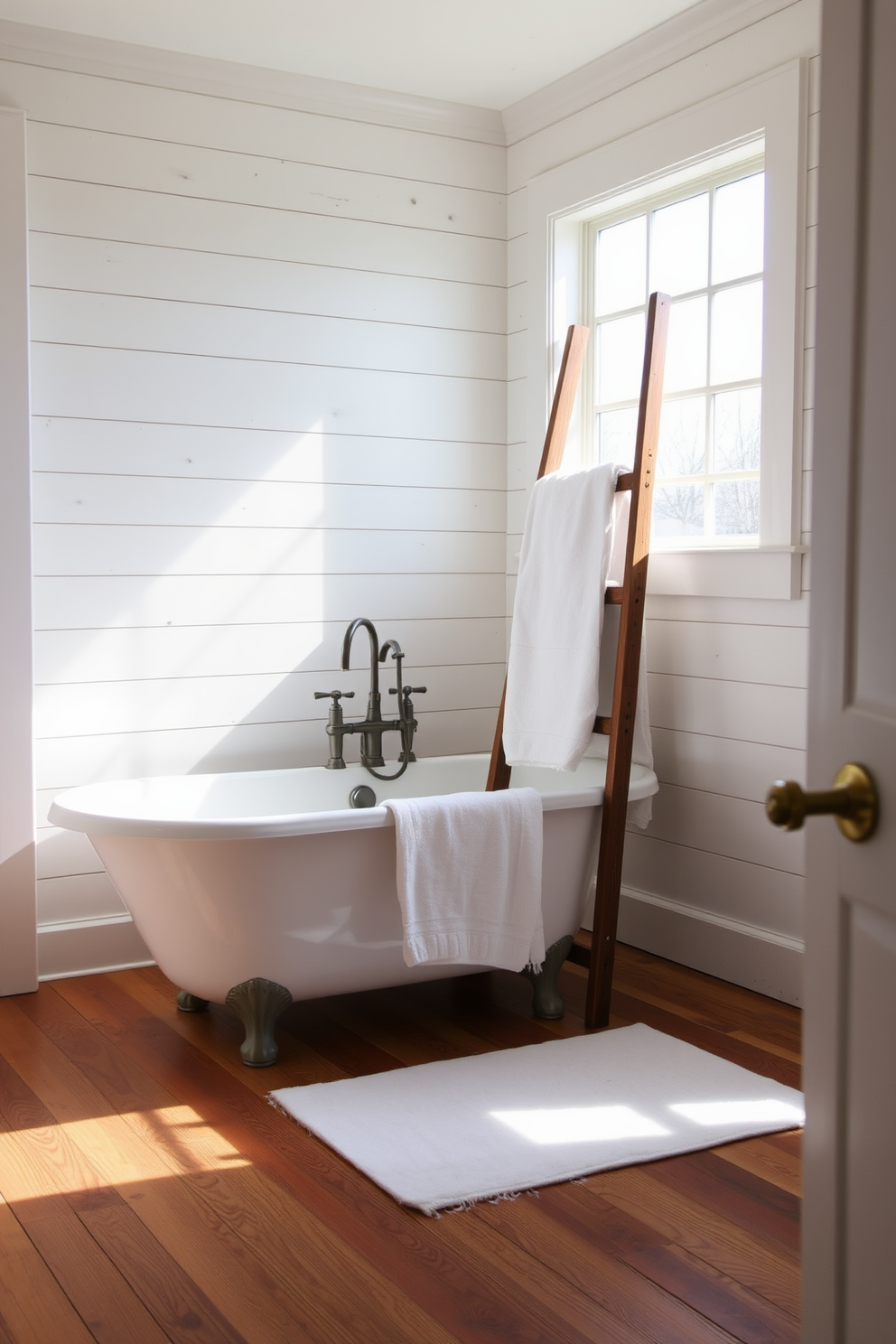 A cozy farmhouse bathroom featuring shiplap walls that exude rustic charm. The space includes a freestanding soaking tub with a vintage-style faucet and a large window allowing natural light to flood in. A wooden ladder is leaned against the wall, holding fluffy white towels. The flooring consists of wide plank wood, adding warmth and character to the design.