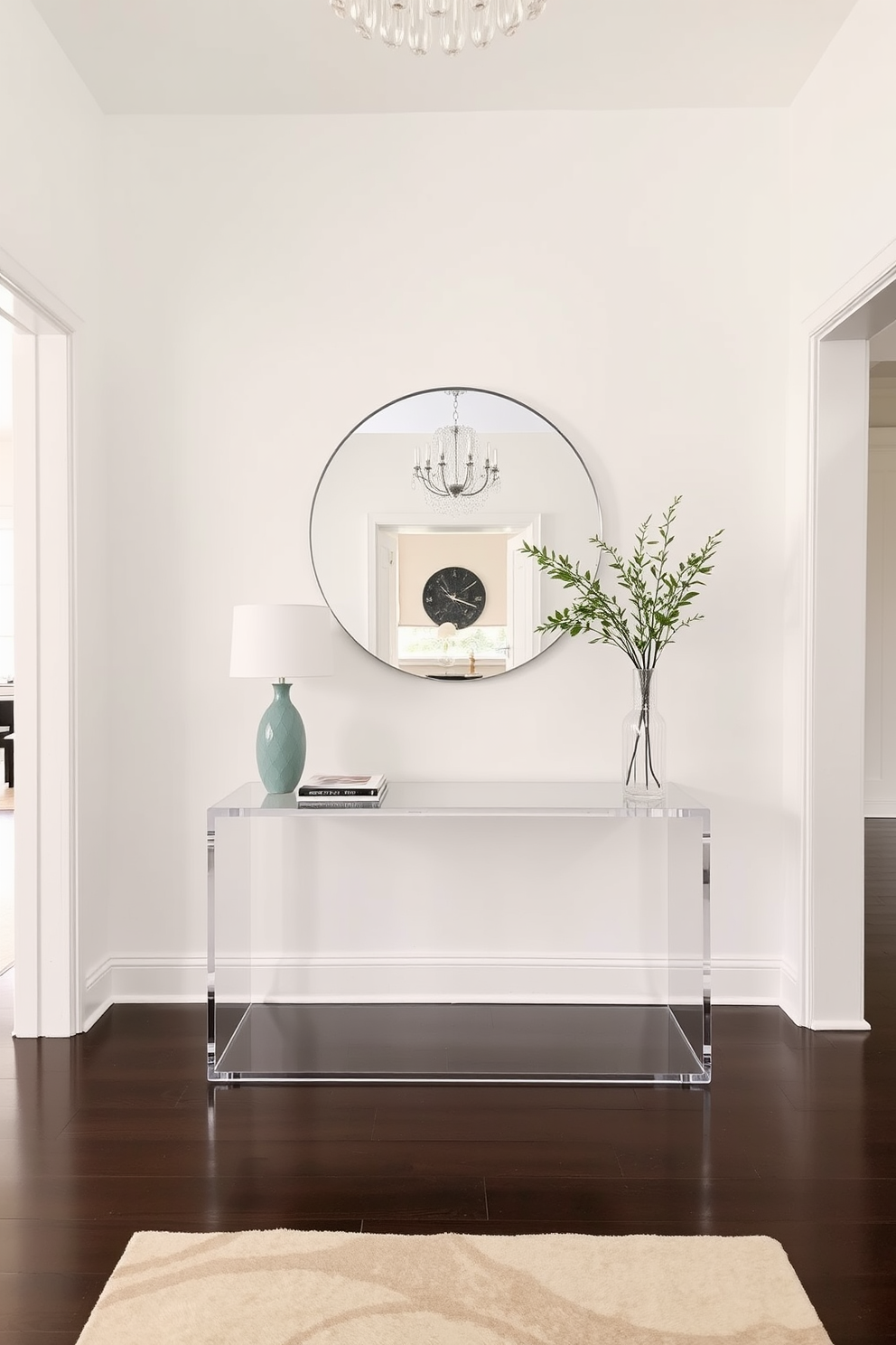 A spacious foyer featuring clear acrylic furniture to enhance the sense of openness. The walls are painted in a soft white hue, and a large round mirror hangs above a minimalist console table made of acrylic.