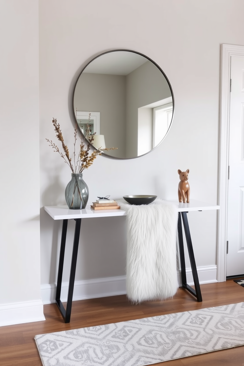 A welcoming foyer featuring a sleek console table with a faux fur runner draped across it. The walls are adorned with soft neutral tones, complemented by a large round mirror that adds depth to the space. A plush area rug with a subtle pattern lies beneath the console, creating a warm and inviting atmosphere. Decorative elements like a vase with seasonal flowers and a stylish key bowl enhance the cozy appeal of the entryway.