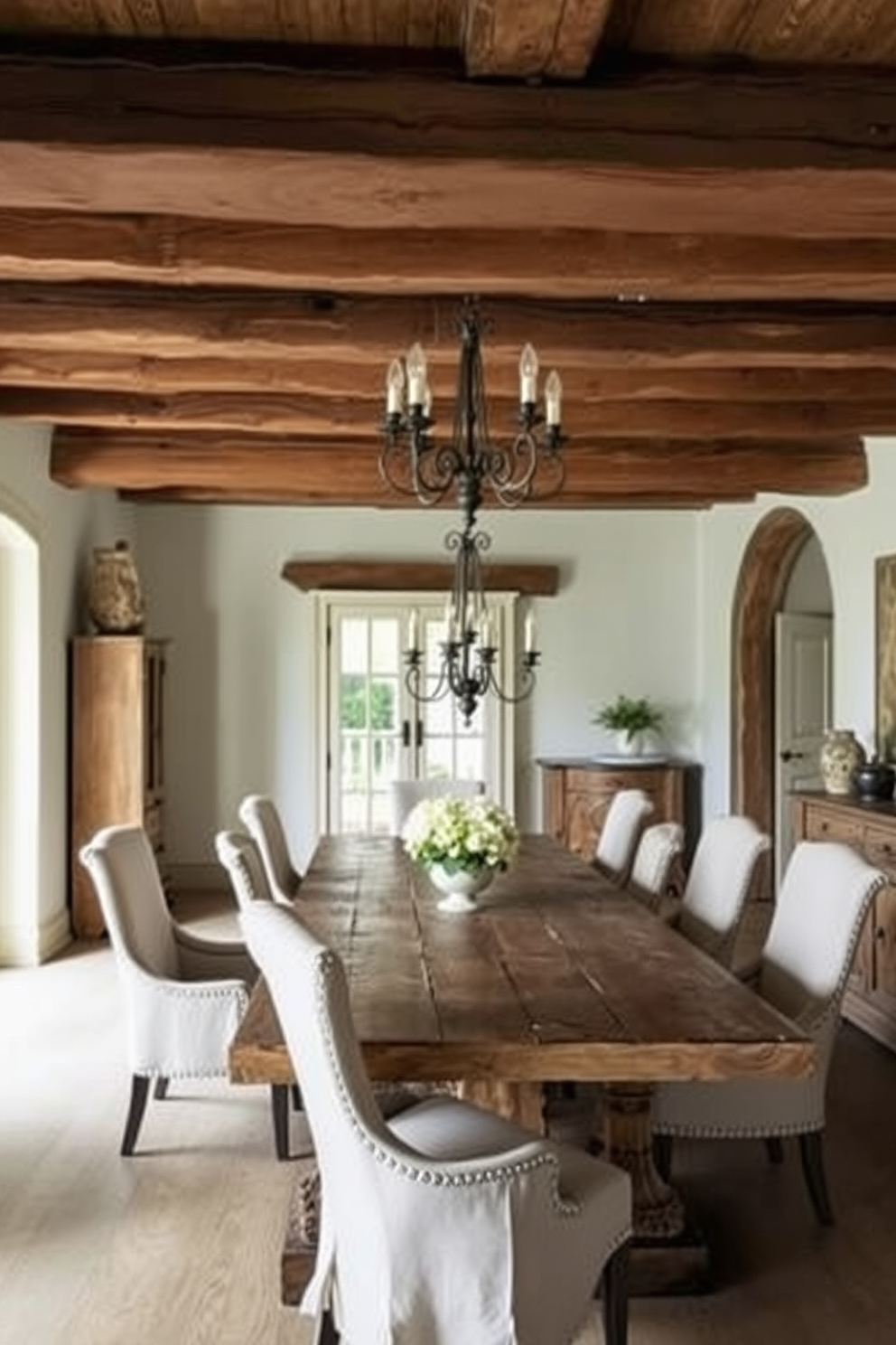 A rustic French dining room features exposed wooden beams that create a warm and inviting atmosphere. The space is adorned with a large farmhouse table surrounded by mismatched vintage chairs, complemented by a cozy fireplace at one end.