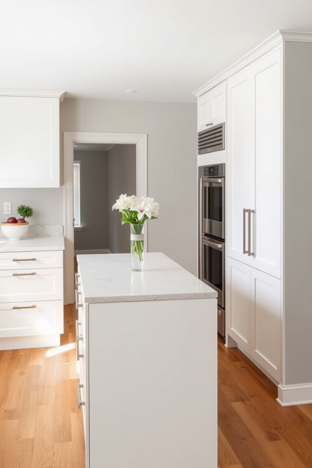 A sleek galley kitchen featuring a slim kitchen island positioned centrally. The cabinetry is a soft white with brushed nickel handles, and the countertops are a polished quartz with subtle veining. On one side of the kitchen, there are stainless steel appliances seamlessly integrated into the cabinetry. The walls are painted in a light gray, and the flooring consists of warm oak planks that add a touch of elegance.