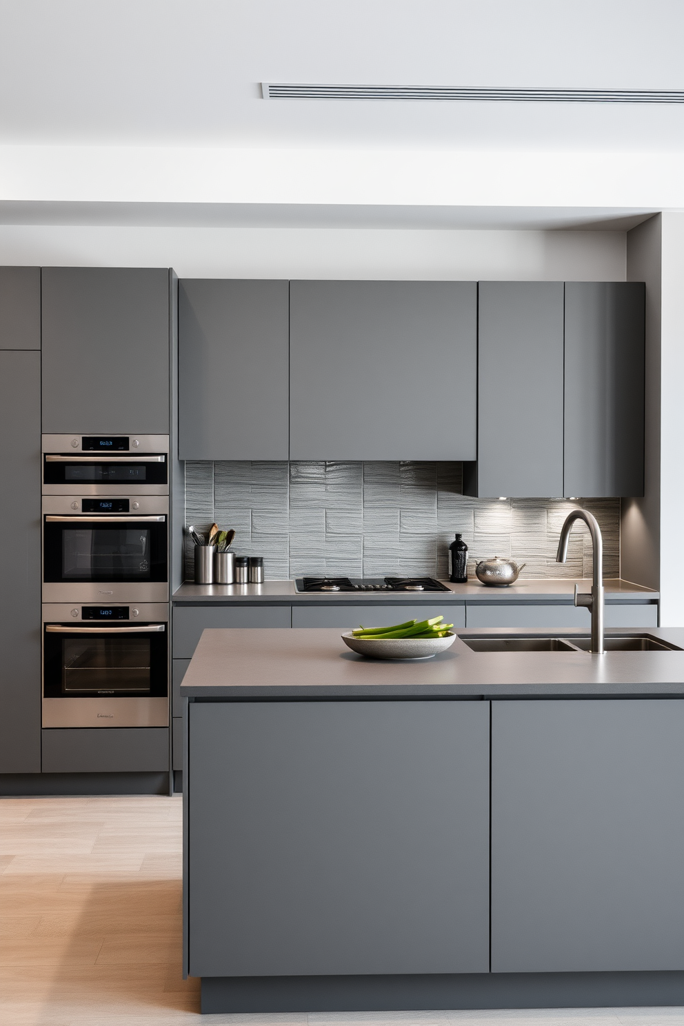 A sleek German kitchen design featuring a monochromatic color scheme in various shades of gray. The cabinetry is minimalistic with clean lines, complemented by a large central island topped with a matching gray countertop. Stainless steel appliances seamlessly blend into the design, enhancing the modern aesthetic. The backsplash consists of textured gray tiles, adding depth to the overall look while maintaining an elegant simplicity.