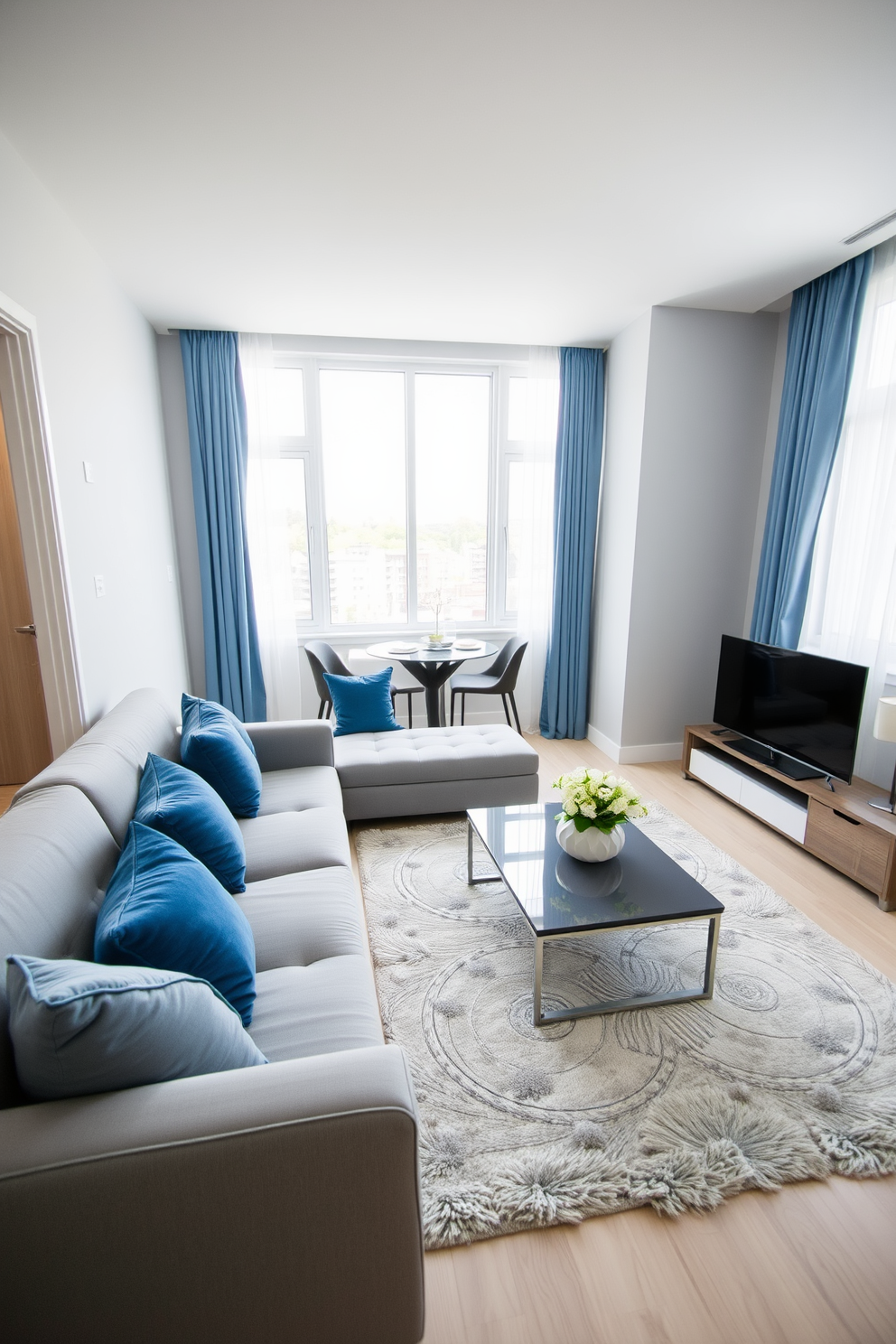 Bright blue accessories contrast beautifully against the soft gray walls of the apartment. The living area features a sleek gray sofa complemented by bright blue throw pillows and a matching blue area rug. In the kitchen, gray cabinetry is accented with blue dishware and decorative vases. The dining table is set with blue placemats and stylish gray chairs, creating a cohesive yet vibrant atmosphere.