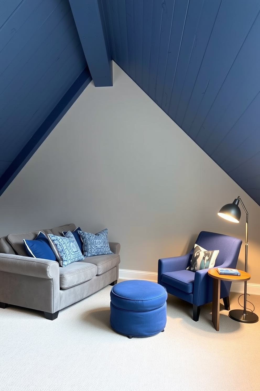 A serene attic room designed with a gray and blue color palette. The walls are painted a soft gray, while the ceiling features exposed wooden beams painted in a deep blue tone. A plush gray sofa is positioned against one wall, adorned with blue accent pillows. A cozy reading nook is created with a blue armchair and a small wooden side table, illuminated by a stylish floor lamp.