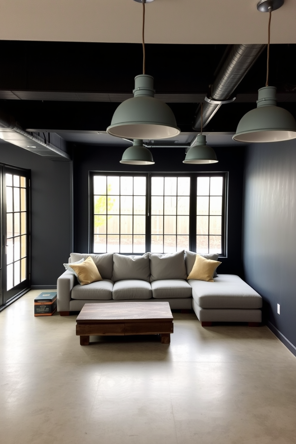 A contemporary basement space featuring industrial gray lighting fixtures that hang low from the ceiling. The walls are painted in a deep charcoal color, and the floor is finished with polished concrete, creating a sleek and modern aesthetic. A cozy seating area is arranged with a sectional sofa in a light gray fabric, complemented by a rustic wooden coffee table. Large windows with black frames allow natural light to filter in, enhancing the industrial vibe of the space.