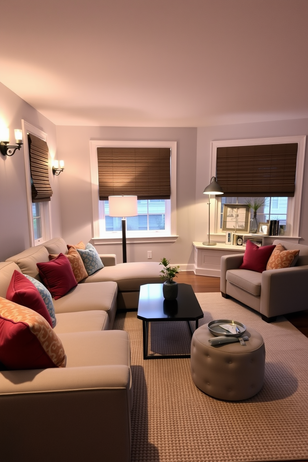 Layered lighting in gray tones creates a cozy and inviting atmosphere in a family room. The space features a plush sectional sofa in a soft gray fabric, accented by colorful throw pillows and a sleek coffee table in the center. Wall sconces with warm light flank the windows, while a stylish floor lamp adds additional illumination in the reading nook. The walls are painted in a light gray hue, complemented by a textured area rug that adds warmth underfoot.