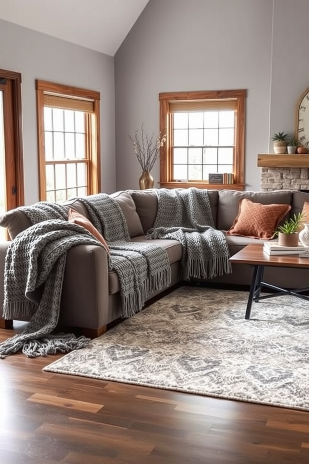 A cozy family room featuring textured gray blankets draped over a plush sectional sofa. The walls are painted in a soft gray hue, complemented by warm wood accents and a large area rug that adds comfort underfoot.