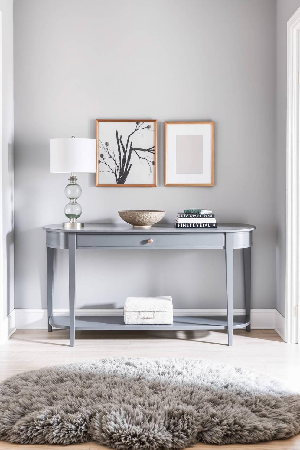 An elegant gray console table is positioned against the wall in a stylish foyer. Above the table, a large decorative mirror with an intricate frame reflects the soft lighting of the space. The walls are painted in a light gray hue, complementing the console's finish, while a plush area rug adds warmth underfoot. A small arrangement of fresh flowers and a few carefully selected decorative items adorn the table, enhancing the foyer's sophisticated ambiance.