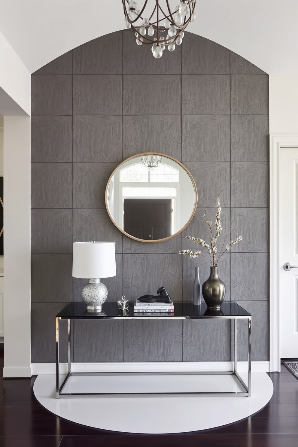 Textured gray wall panels create a striking focal point in the foyer. The space features a sleek console table with decorative accents and a large round mirror that enhances the room's depth.