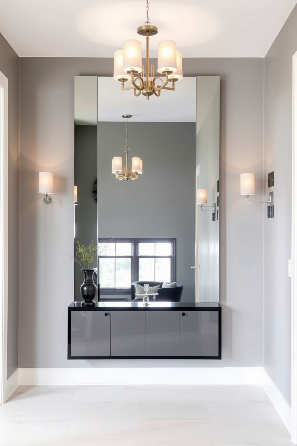 A sleek gray wall mirror is the focal point of the foyer, enhancing the sense of space and depth. The walls are painted in a soft gray hue, complemented by elegant lighting fixtures that create a warm and inviting atmosphere.