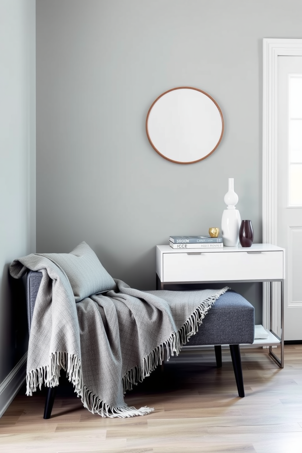 A cozy foyer featuring layered gray throw blankets draped over a stylish bench. The walls are painted in a soft gray hue, complemented by a sleek console table adorned with decorative accents.