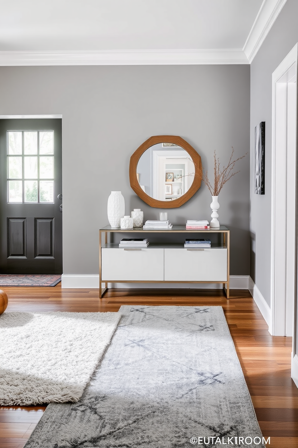 A stylish foyer featuring layered gray rugs that add a cozy texture to the space. The walls are painted in a soft gray hue, complemented by a sleek console table adorned with decorative items and a statement mirror above it.