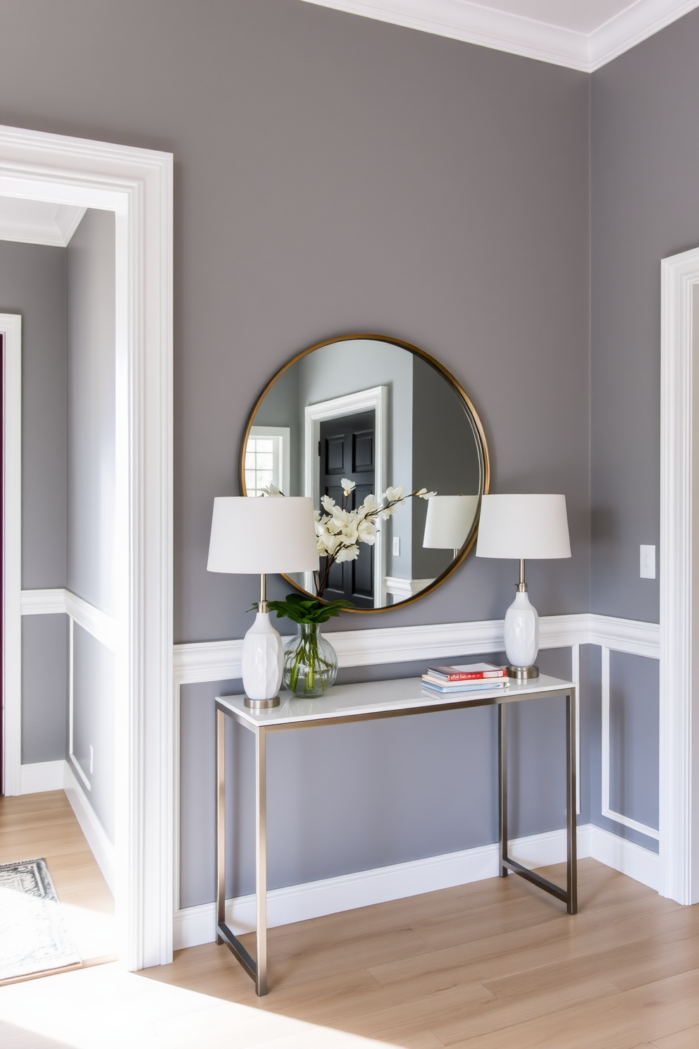 A stylish foyer featuring gray painted walls complemented by crisp white trim. The space is adorned with a sleek console table and a large round mirror, creating an inviting atmosphere.