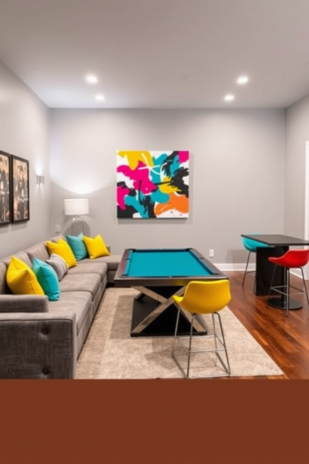 A stylish game room featuring a gray color palette accented with vibrant pops of color. The walls are painted a soft gray, complemented by a plush gray sectional sofa adorned with bright throw pillows in shades of yellow and teal. A sleek pool table sits in the center of the room, surrounded by contemporary bar stools in bold colors. The flooring is a rich hardwood, and a large piece of abstract art with vivid hues hangs above the sofa, tying the space together.