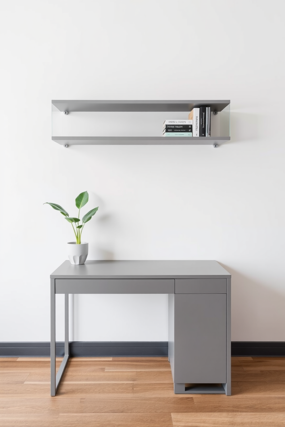 A minimalist gray desk is positioned against a soft white wall, complemented by sleek floating shelves above it. The desk features clean lines and a simple design, while the shelves display curated books and a small potted plant for a touch of greenery.