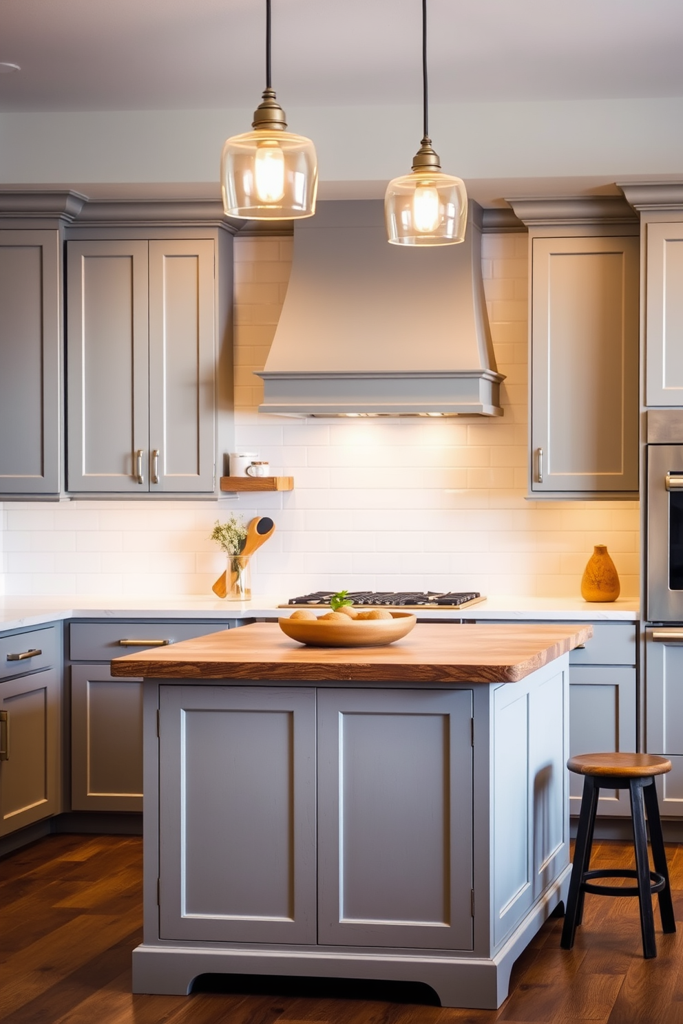 A warm gray kitchen setting featuring natural wood accents. The cabinets are a soft gray with a matte finish, complemented by a rustic wooden island topped with a light marble surface. The backsplash consists of white subway tiles, creating a clean and classic look. Pendant lights with a warm glow hang above the island, illuminating the space beautifully.