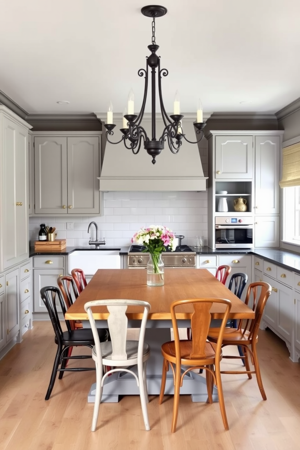 An elegant gray kitchen featuring vintage touches. The cabinetry is a soft gray with antique brass hardware, complemented by a farmhouse sink and a classic subway tile backsplash. A large wooden dining table sits in the center, surrounded by mismatched vintage chairs. The room is illuminated by a wrought iron chandelier that adds a warm, inviting glow to the space.