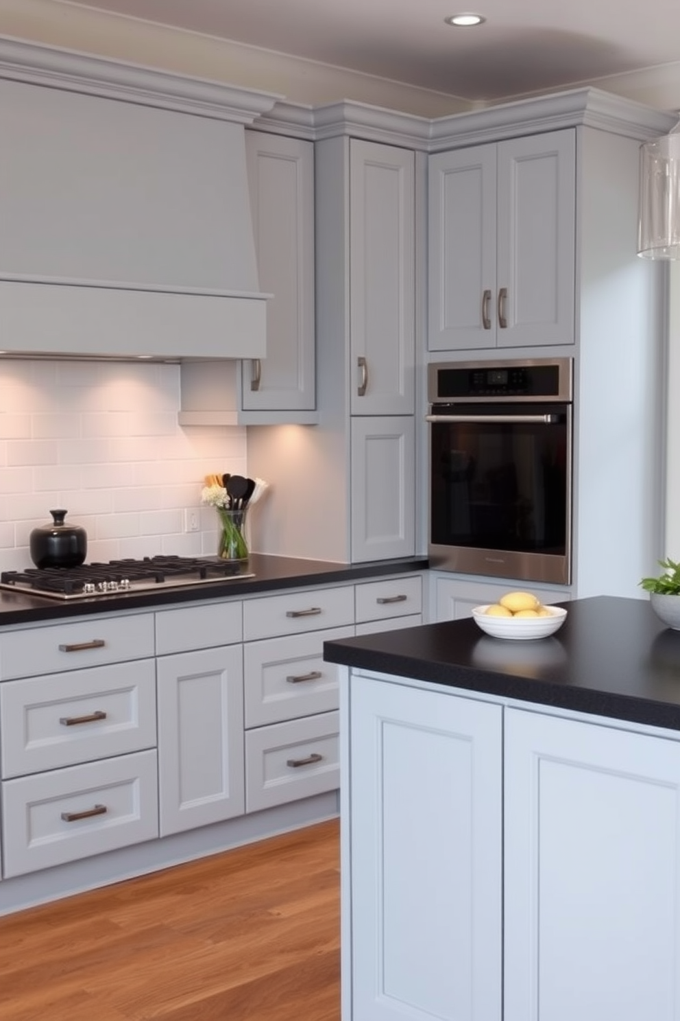 A modern gray kitchen featuring sleek cabinets that contrast beautifully with dark, polished countertops. The space is illuminated by pendant lights hanging above an island, creating a warm and inviting atmosphere. The backsplash consists of white subway tiles that add a touch of brightness to the overall design. Stainless steel appliances complete the contemporary look, while a bowl of fresh fruits sits on the countertop for a pop of color.