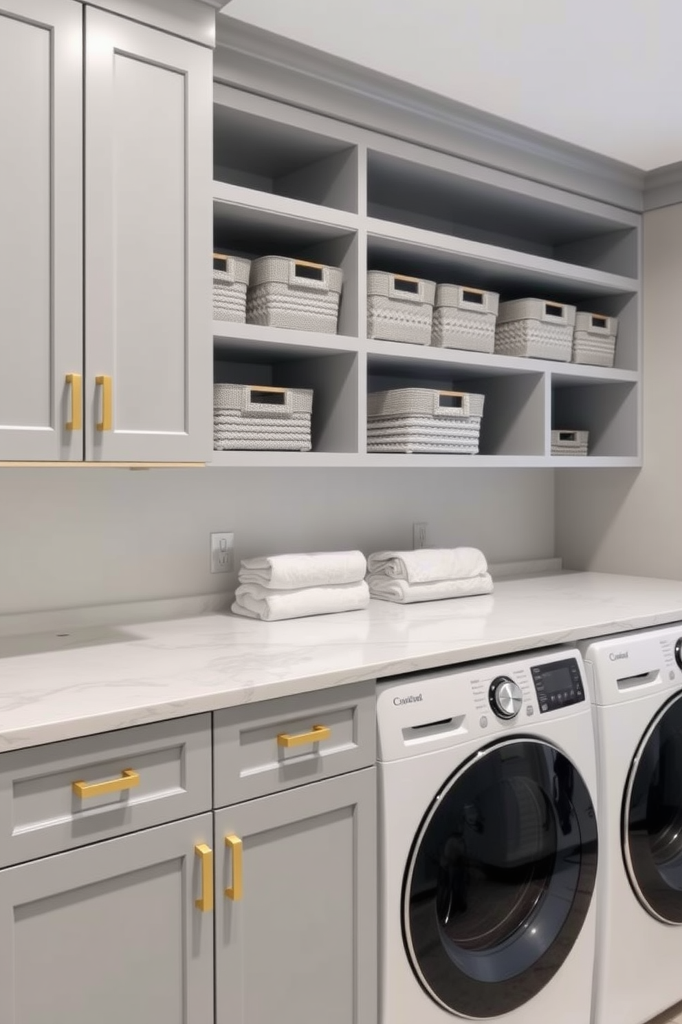 A modern laundry room featuring a gray color scheme with gold accents. The walls are painted a soft gray, complemented by sleek gold hardware on the cabinets. A spacious countertop made of white quartz provides ample space for folding clothes. Decorative storage baskets in various shades of gray are neatly arranged on the shelves for organization.