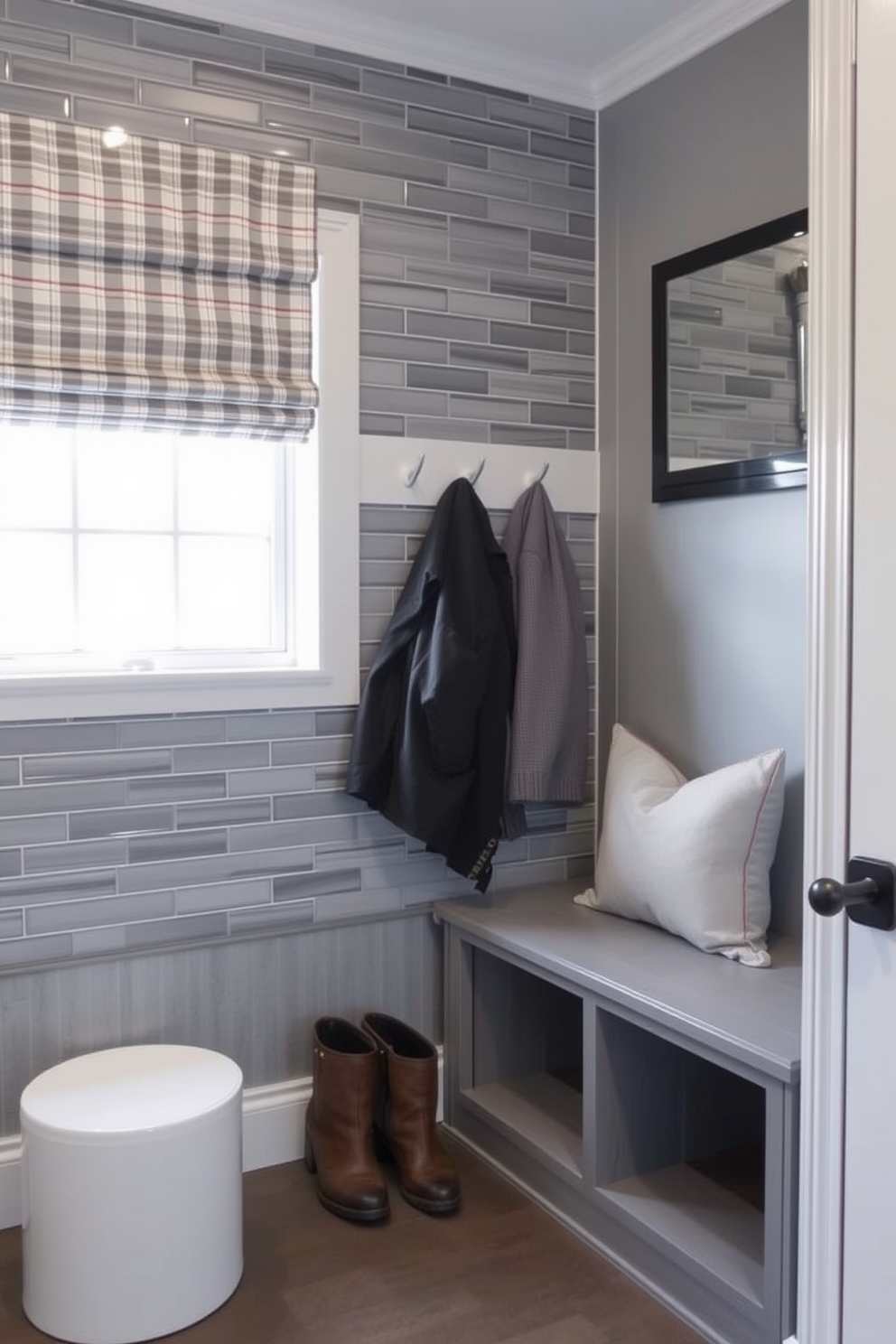 A contemporary gray coat rack stands against the wall, featuring sleek lines and a minimalist design. Below the rack, a matching bench provides a comfortable spot to sit while putting on or taking off shoes. The mudroom is designed with a soft gray color palette, accented by natural wood elements for warmth. A durable yet stylish rug lies beneath the bench, adding texture and inviting comfort to the space.