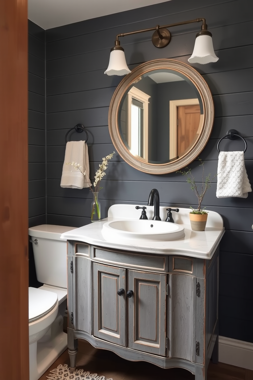 A cozy gray powder room with dark gray shiplap walls creating a rustic ambiance. The space features a vintage wooden vanity with a white ceramic sink and a large round mirror framed in distressed wood.