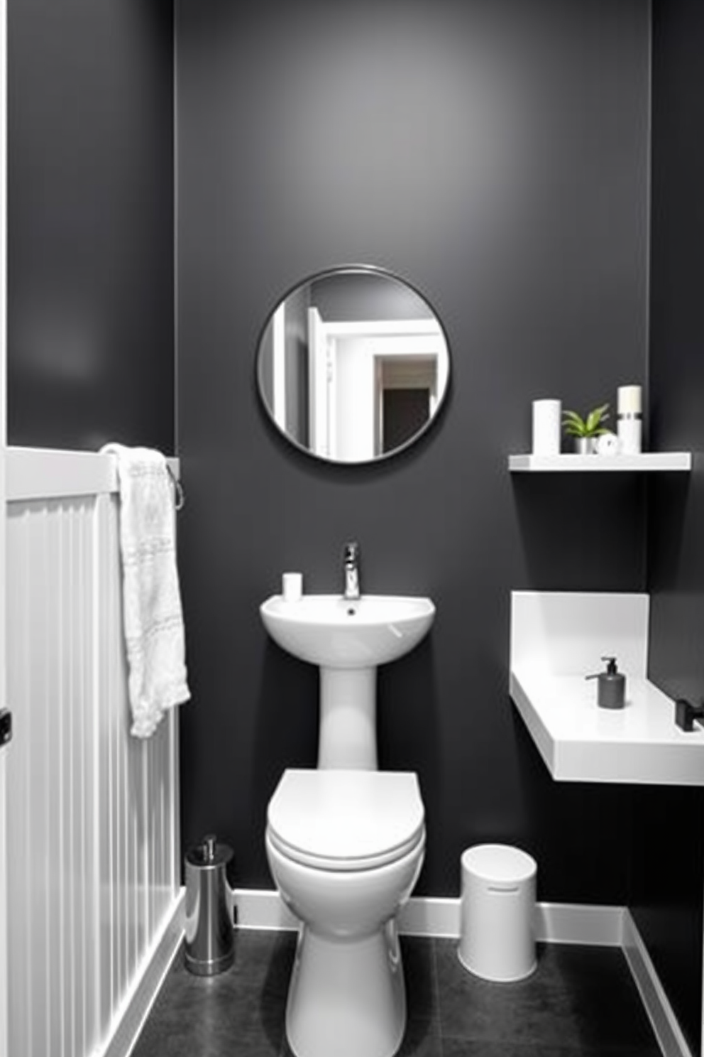 Charcoal gray walls create a bold backdrop for a stylish powder room. The space features sleek white fixtures, including a modern pedestal sink and a compact toilet, enhancing the room's contemporary feel. To the right of the sink, a minimalist floating shelf displays elegant decor items. A round mirror with a thin black frame hangs above the sink, reflecting the sophisticated color palette.