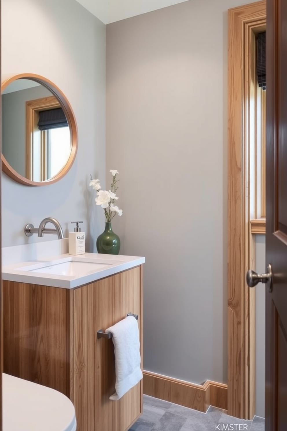 A soft gray powder room featuring natural wood accents creates a serene and inviting atmosphere. The walls are painted in a soft gray shade, complemented by a wooden vanity with a sleek countertop, enhancing the overall aesthetic. Stylish fixtures in brushed nickel add a touch of elegance to the space. A round mirror with a wooden frame hangs above the vanity, reflecting the warm tones of the wood and the soft gray walls.