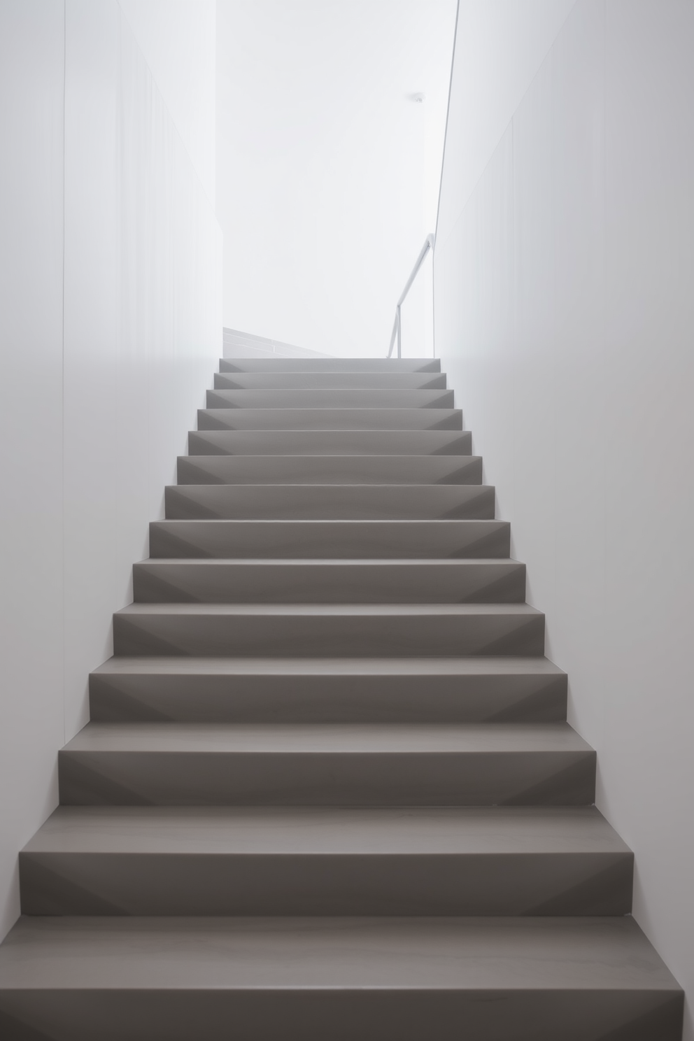 A gray concrete staircase with a smooth finish leads elegantly to the upper level. The design features clean lines and a minimalist aesthetic, complemented by soft lighting that highlights the staircase's contours.