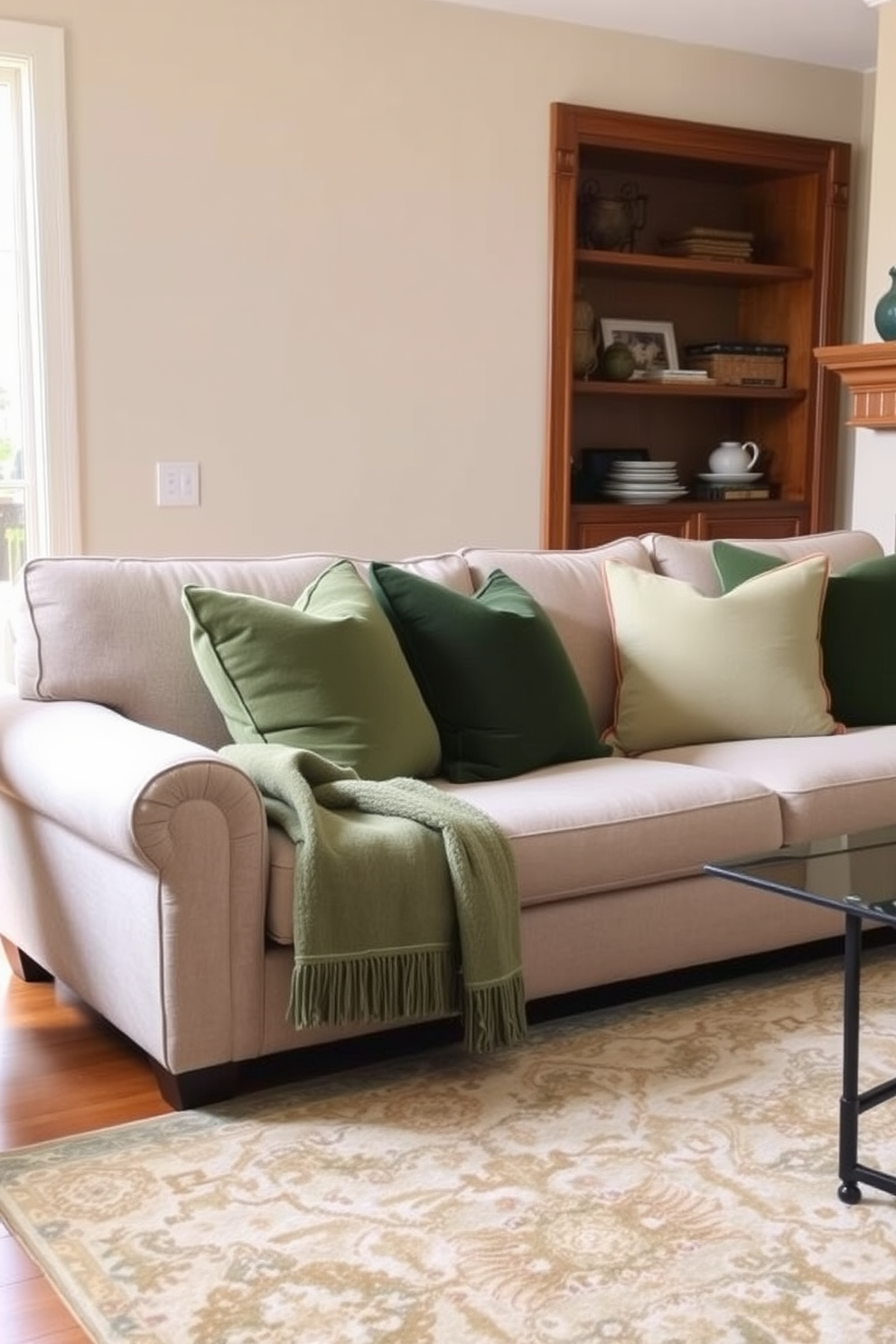 A cozy family room featuring a plush couch adorned with layered green throw pillows in varying shades. The walls are painted a soft beige, complemented by warm wooden accents and a large area rug that adds texture to the space.