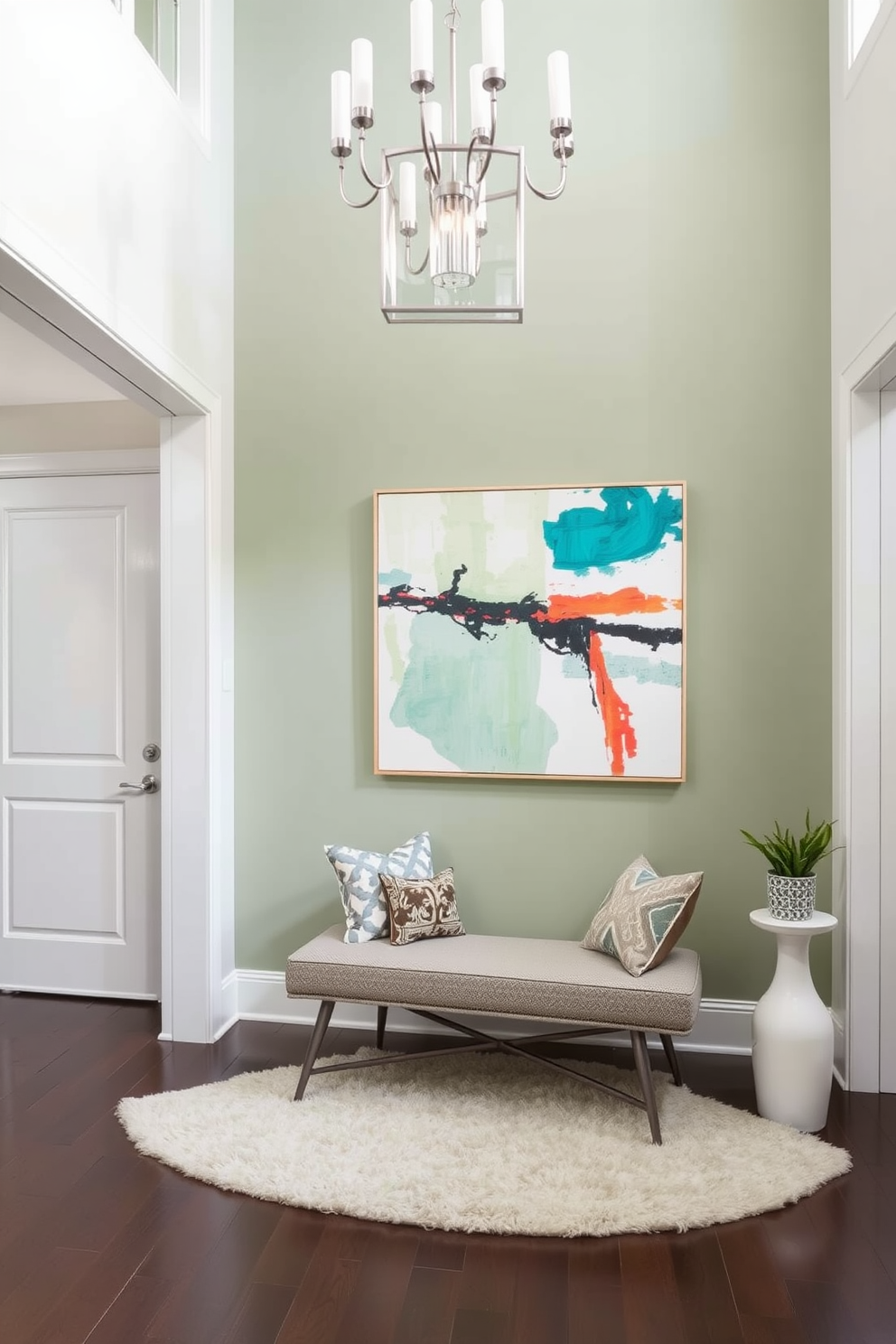 A serene foyer featuring a sage green accent wall adorned with a large abstract artwork that adds a pop of color. The space is illuminated by a stylish chandelier, while a plush area rug anchors the seating arrangement with a modern bench and decorative cushions.